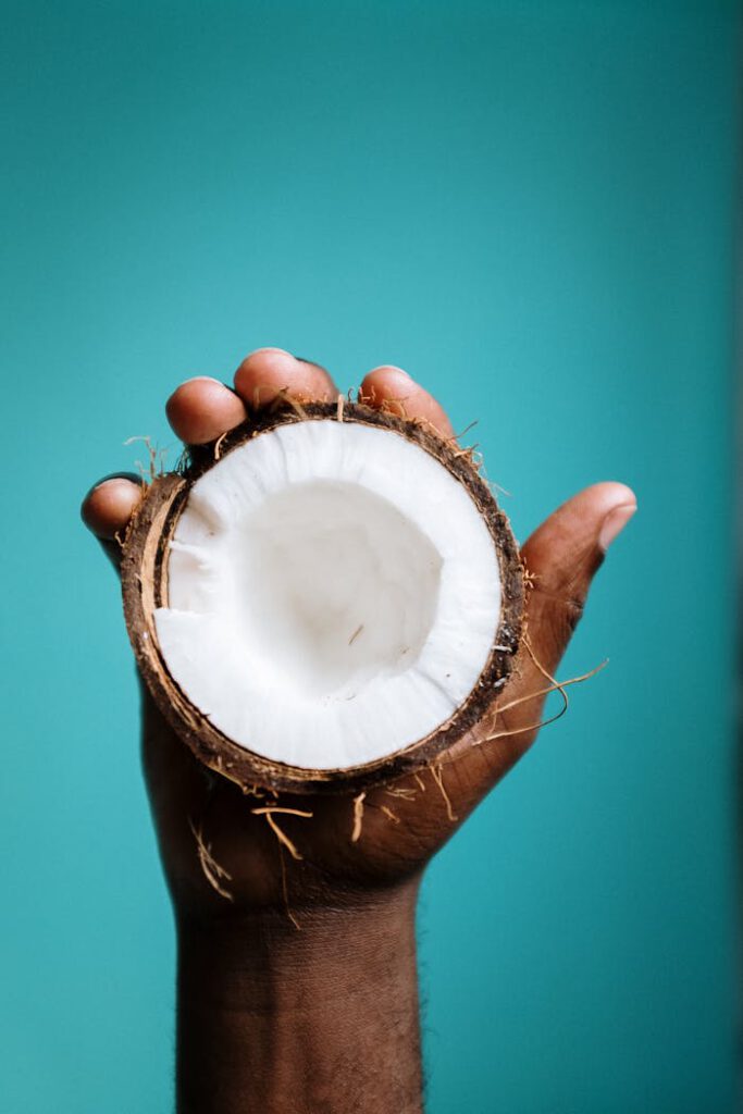 Close-up of a hand holding a halved coconut against a vibrant blue background.